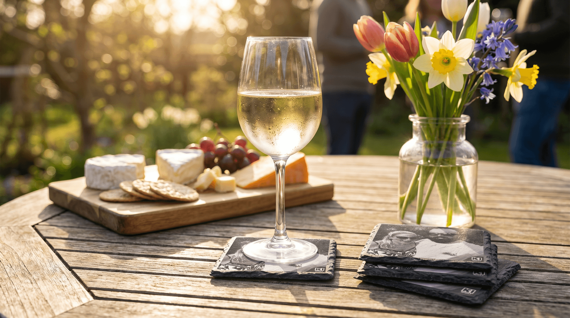 Garden bank-holiday table with personalised slate coasters, a cookbook and a glass of wine in spring sunshine