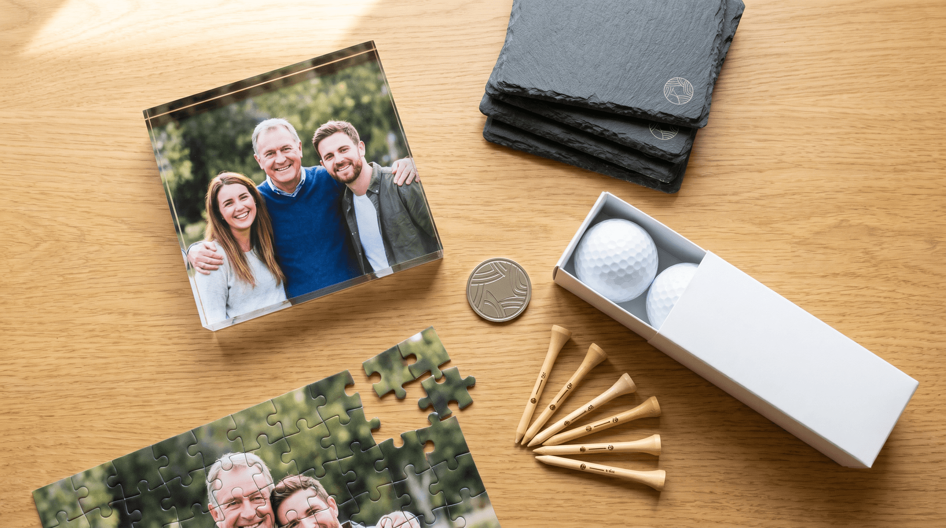 Father's Day gift selection under £25 — engraved ball marker, slate coasters, photo block and personalised golf balls on a wooden desk