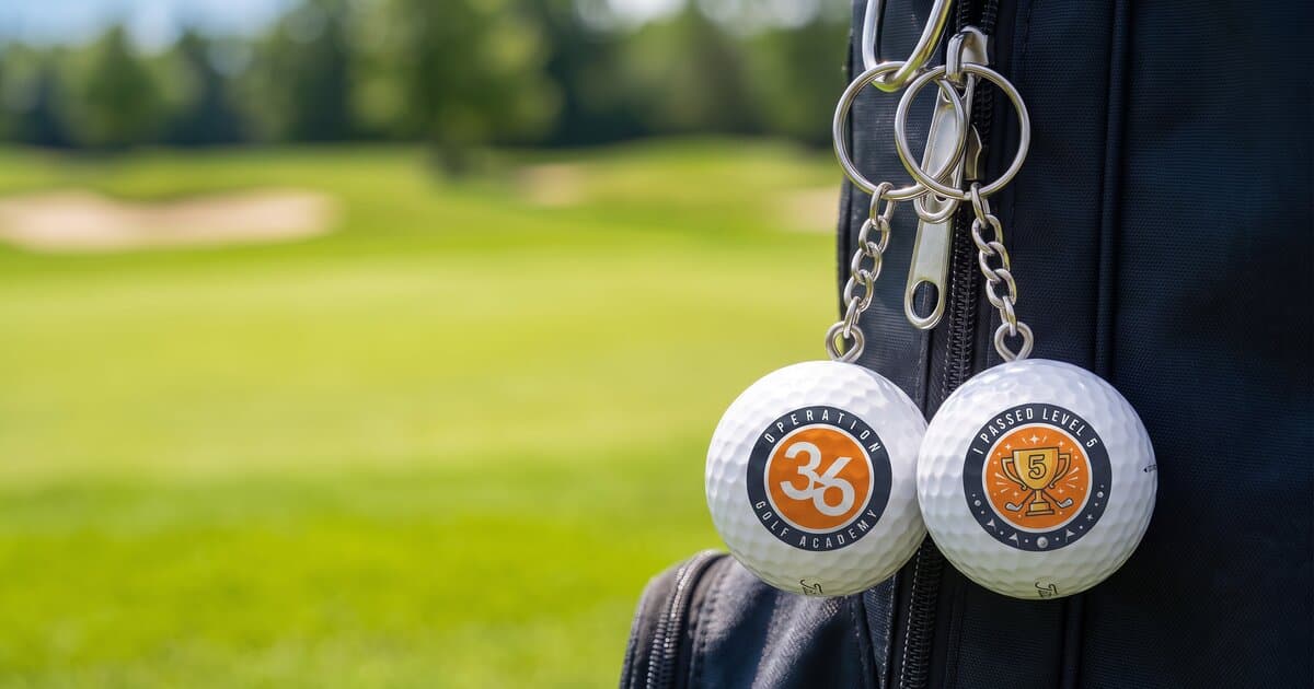 Two personalised golf ball keyrings hanging from a golf bag on a course, one with the Operation 36 Golf Academy logo and one reading I Passed Level 5