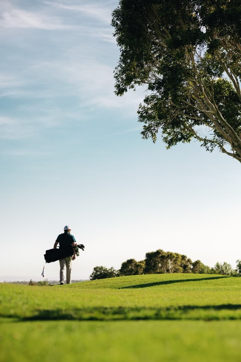 Golfer walking down fairway with golf bag on sunny day