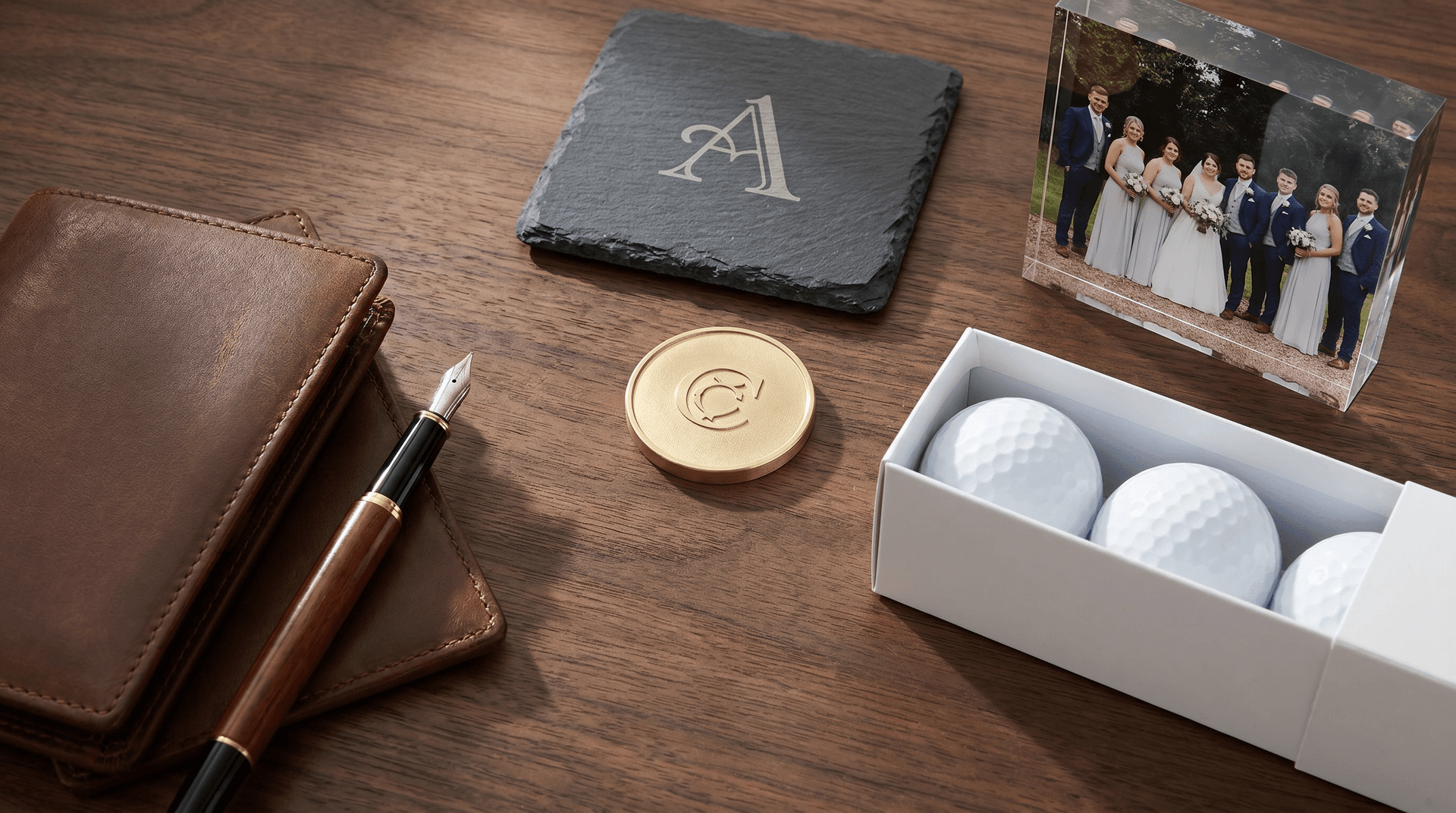 Engraved ball marker coin, slate coasters, photo block and golf balls arranged on a dark wood desk as personalised groomsmen gifts