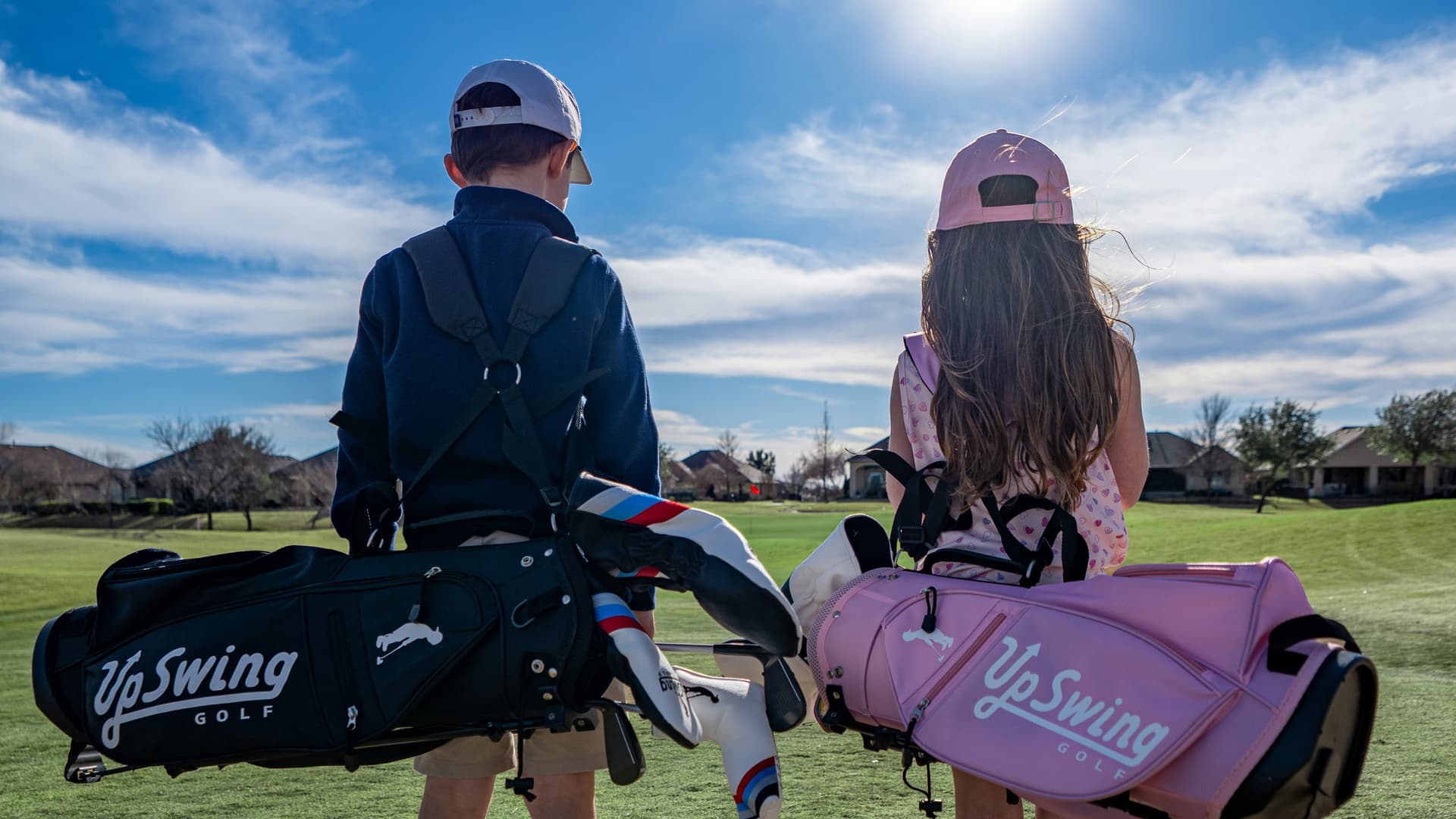 Two junior golfers walking down a fairway carrying Upswing junior golf bags