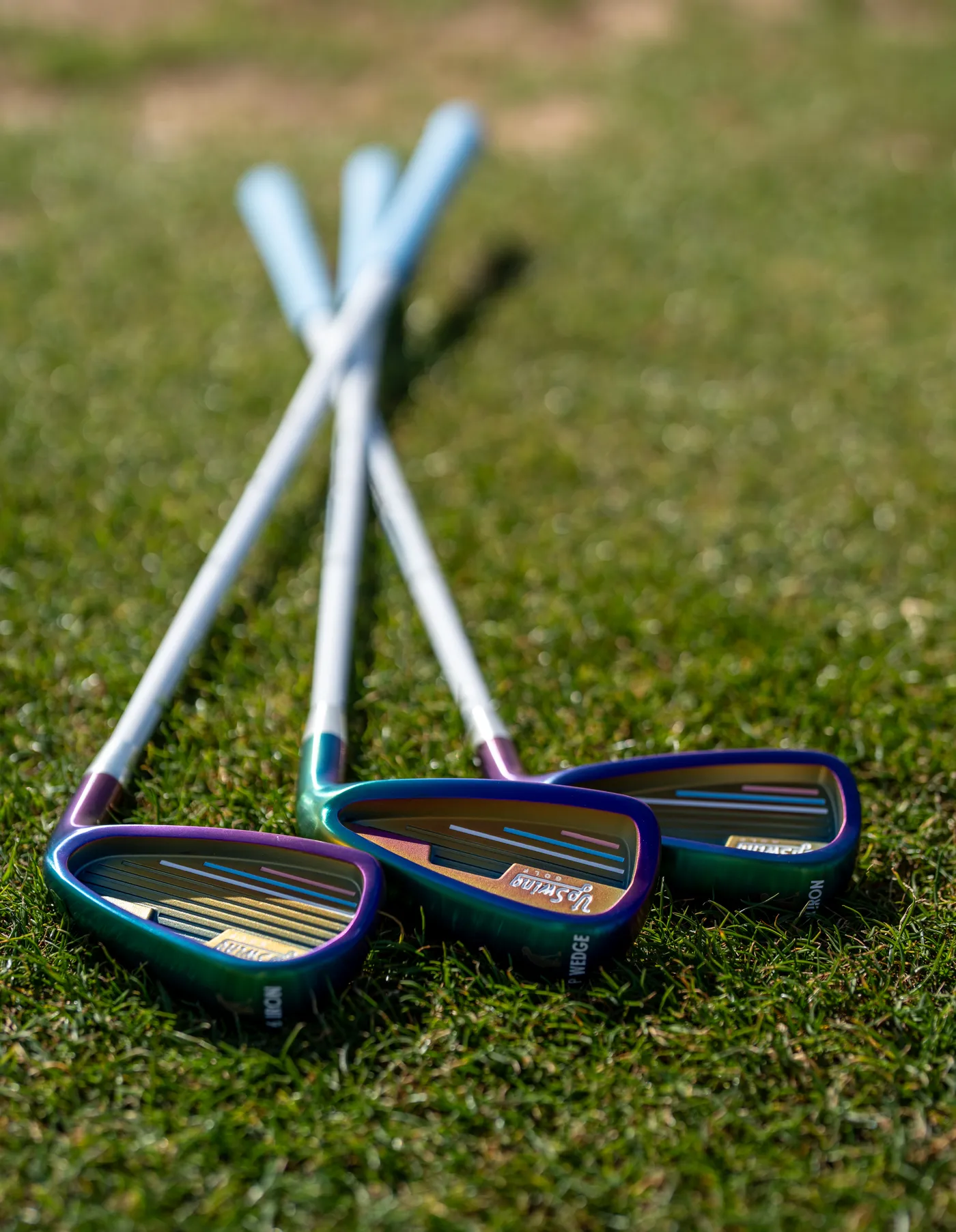 Three Upswing Galaxy junior irons on grass, showing the iridescent green and violet finish