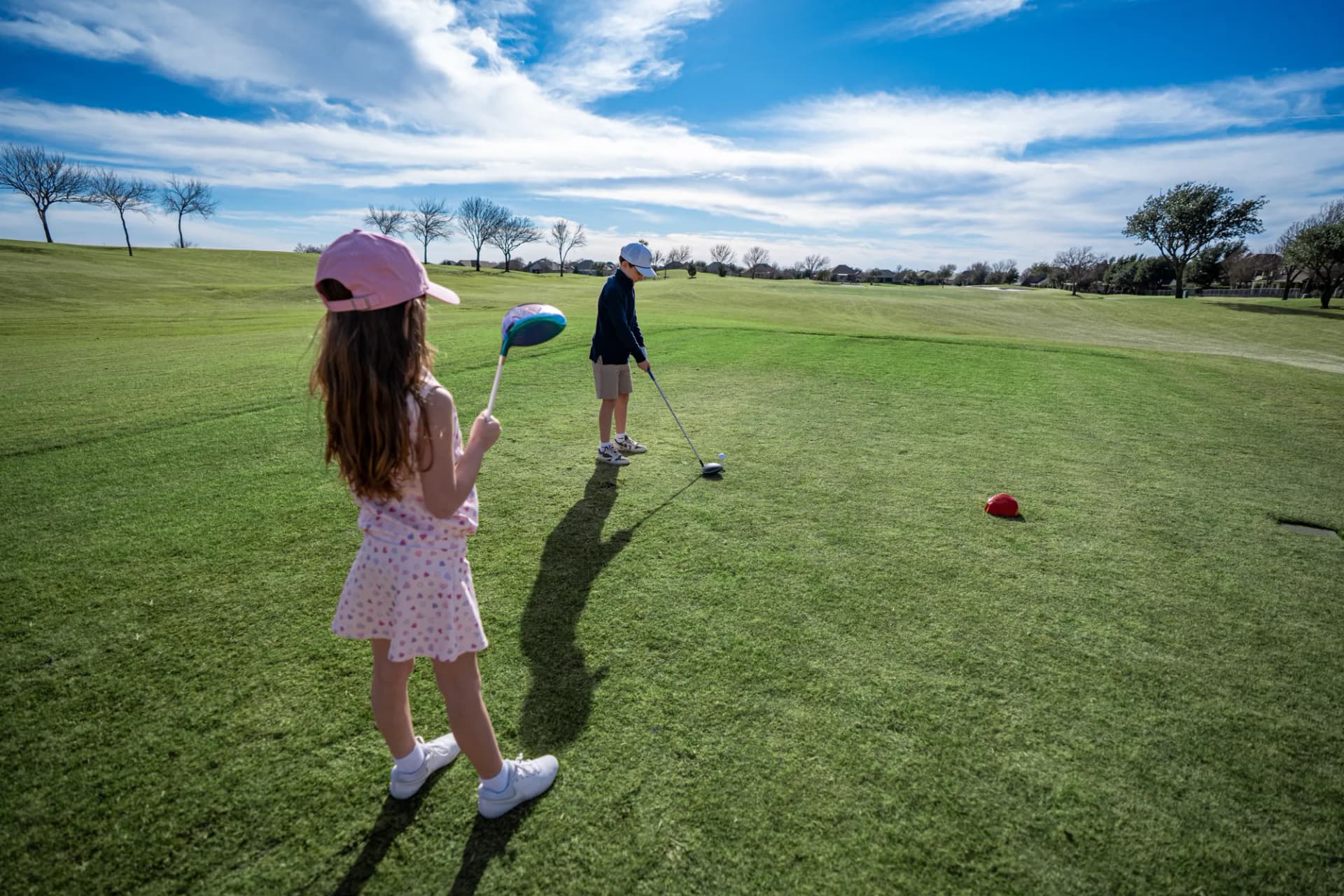 Two junior golfers on the tee, one addressing the ball with an Upswing driver